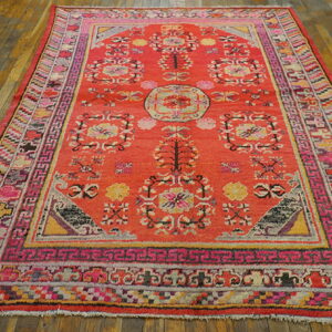 Coral area rug with elaborate borders and pink, yellow, and gray floral patterns on wood planks.