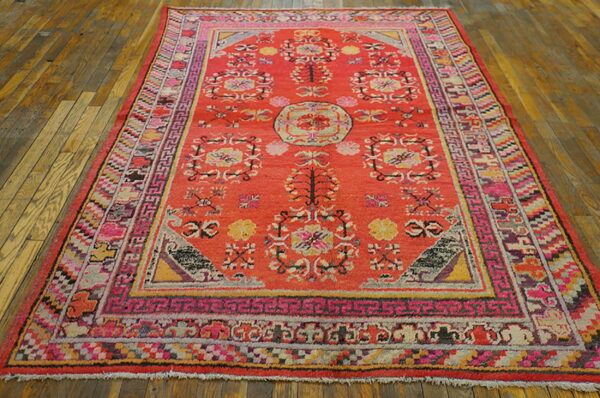 Coral area rug with elaborate borders and pink, yellow, and gray floral patterns on wood planks.