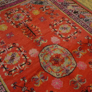 Thick pile red rug with detailed pink, purple, and green traditional designs on a wood plank floor.