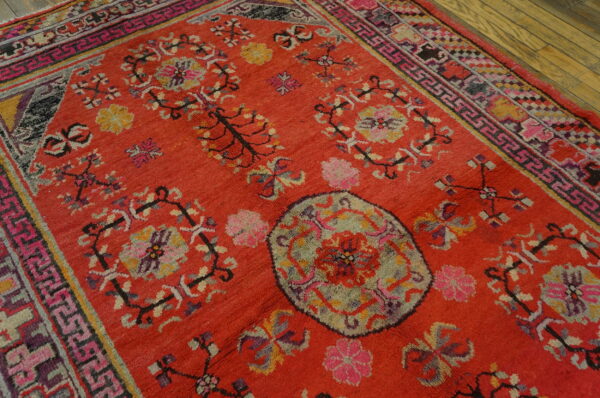 Thick pile red rug with detailed pink, purple, and green traditional designs on a wood plank floor.