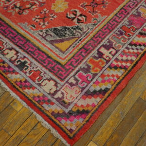 Colorful patterned rug corner featuring red, pink, yellow, and gray borders on distressed wooden flooring.