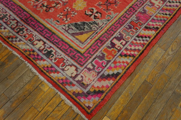 Colorful patterned rug corner featuring red, pink, yellow, and gray borders on distressed wooden flooring.