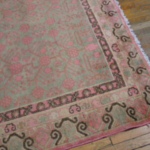 Pink and muted green rug featuring intricate floral designs and dark scrolling borders on hardwood planks.