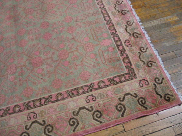 Pink and muted green rug featuring intricate floral designs and dark scrolling borders on hardwood planks.
