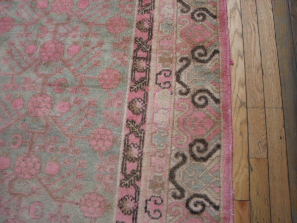 Muted pink and sage green rug featuring repeating floral motifs and decorative borders on hardwood flooring.
