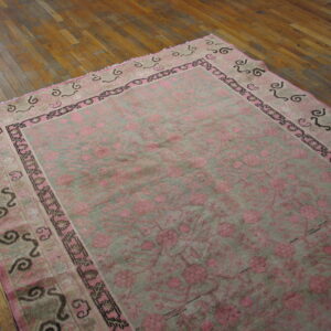 Distressed pink and gray-green floral rug with detailed borders sits on warm hardwood flooring.
