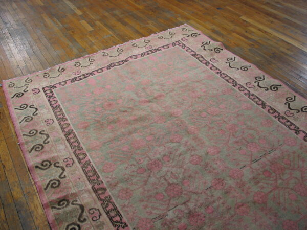 Distressed pink and gray-green floral rug with detailed borders sits on warm hardwood flooring.