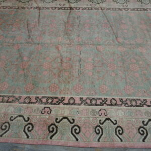 Muted pink and pale green floral rug with multi-layered borders rests on distressed gray wood flooring.
