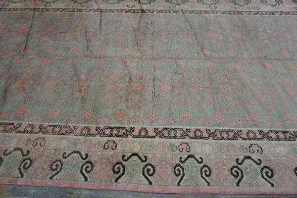 Muted pink and pale green floral rug with multi-layered borders rests on distressed gray wood flooring.