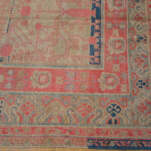 Tan, coral, and navy blue flatweave rug with traditional patterns displayed on a hardwood floor.