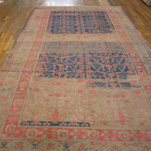 Large rug with complex coral and blue paneled patterns rests on glossy wood flooring.