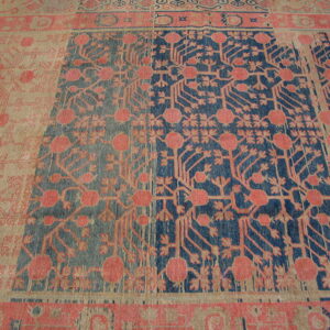 Close-up of a rug with pink floral patterns on alternating blue and beige rectangular panels.