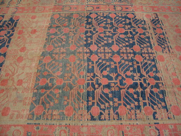 Close-up of a rug with pink floral patterns on alternating blue and beige rectangular panels.