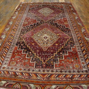 Geometric medallion rug in deep reds, burgundy, and dark brown lies on polished wooden floorboards.