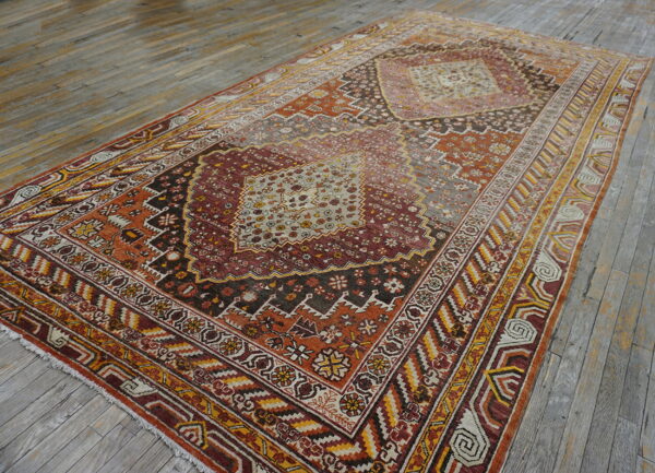 Distressed rug with intricate red, orange, and gold geometric patterns centered on wide gray hardwood planks.