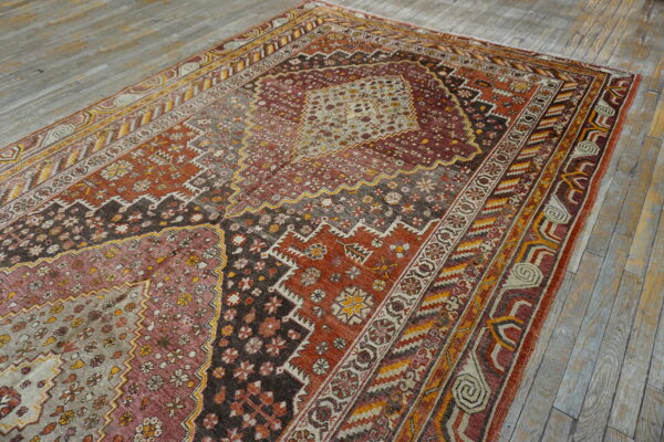 Geometric central medallion rug in earth tones, burgundy, and gold accents rests on weathered wood planks.