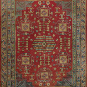 Rust red rug with intricate geometric and stylized botanical designs in teal, gold, blue, and pink.