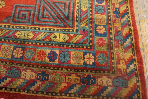 Geometric and floral patterned rug corner features red, teal, gold, and olive colors on distressed wood flooring.