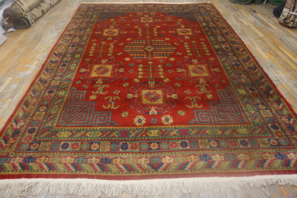Large red rug featuring intricate geometric and stylized botanical patterns in gold, green, and blue on wood planks.
