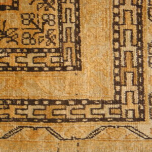 Detail view of a textured gold rug with dark brown geometric border and field motifs.