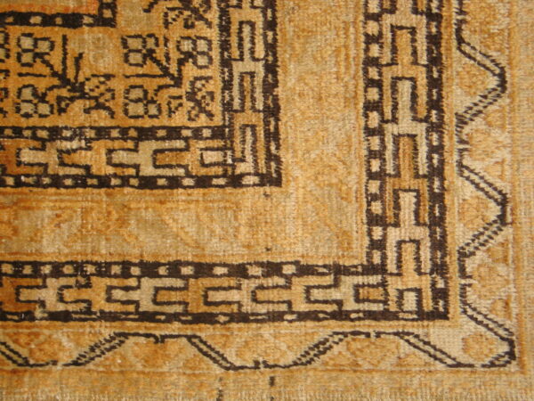 Detail view of a textured gold rug with dark brown geometric border and field motifs.