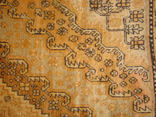 Textured rug close-up showing golden-brown and tan colors with complex stepped geometric designs.