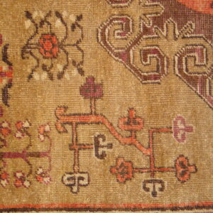 Geometric and stylized floral patterns in brown, red, and purple stand out on the golden-tan rug pile.