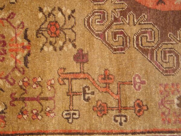 Geometric and stylized floral patterns in brown, red, and purple stand out on the golden-tan rug pile.