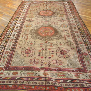 Oversized low-pile rug featuring geometric medallions and borders in beige, rust, and dark brown on hardwood flooring.