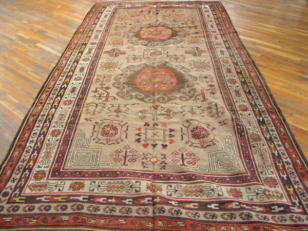 Oversized low-pile rug featuring geometric medallions and borders in beige, rust, and dark brown on hardwood flooring.