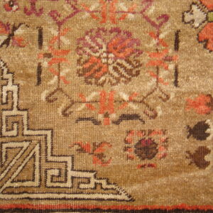 Close-up of a tan, textured rug showing rust, brown, and magenta floral motifs near an angular geometric border.