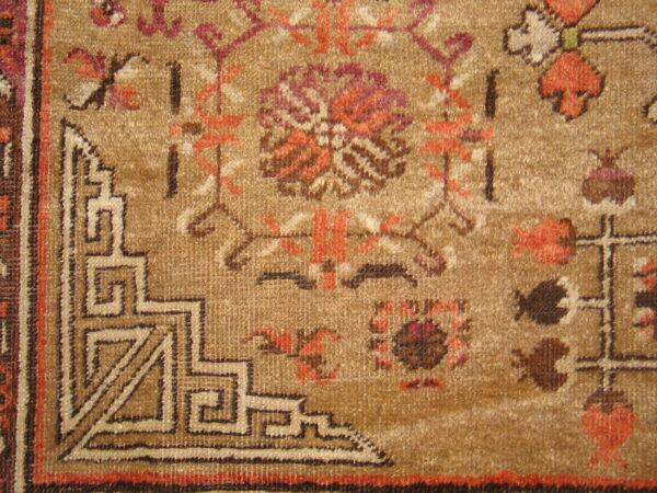 Close-up of a tan, textured rug showing rust, brown, and magenta floral motifs near an angular geometric border.
