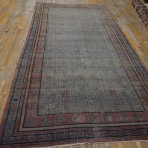 Distressed blue and rust low-pile rug with floral borders lies on aged, wide-plank wood flooring.