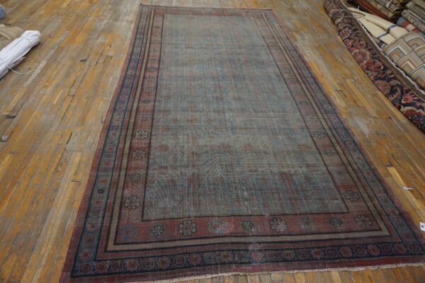 Distressed blue and rust low-pile rug with floral borders lies on aged, wide-plank wood flooring.