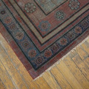 The border of a faded red and blue patterned rug rests diagonally on distressed wooden floorboards.