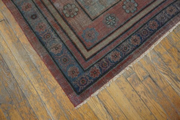 The border of a faded red and blue patterned rug rests diagonally on distressed wooden floorboards.