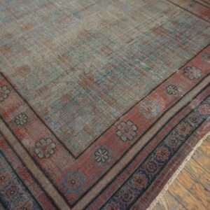 Low-pile rug with a faded blue field and a rust floral medallion border resting on wood flooring.