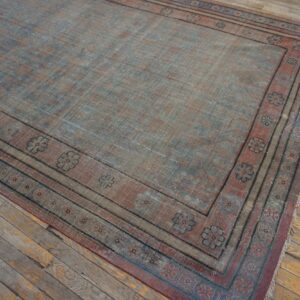 Distressed, low-pile rug in dusty blue and rust with a repeating flower border on rustic wood floors.