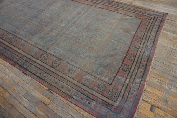 Distressed, low-pile rug in dusty blue and rust with a repeating flower border on rustic wood floors.