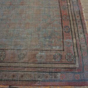 Distressed blue and red traditional rug with floral borders resting on worn yellow and gray wood flooring.