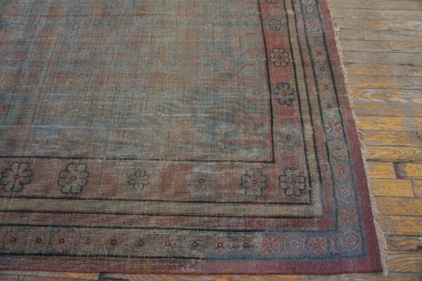 Distressed blue and red traditional rug with floral borders resting on worn yellow and gray wood flooring.