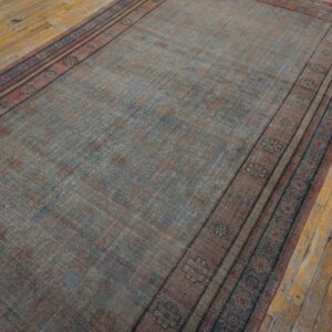 Faded runner rug in blue and reddish-brown with patterned borders resting on distressed wooden floorboards.