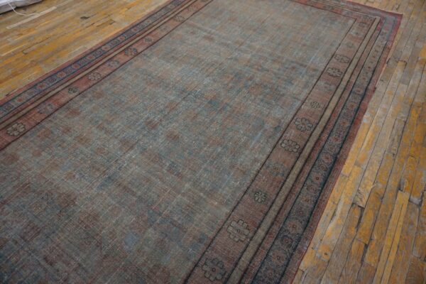 Faded runner rug in blue and reddish-brown with patterned borders resting on distressed wooden floorboards.