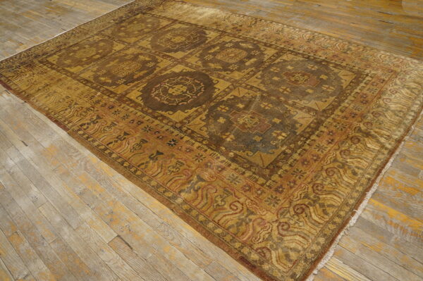 Traditional yellow-gold and dark brown rug with a repeating geometric field lies on distressed plank flooring.