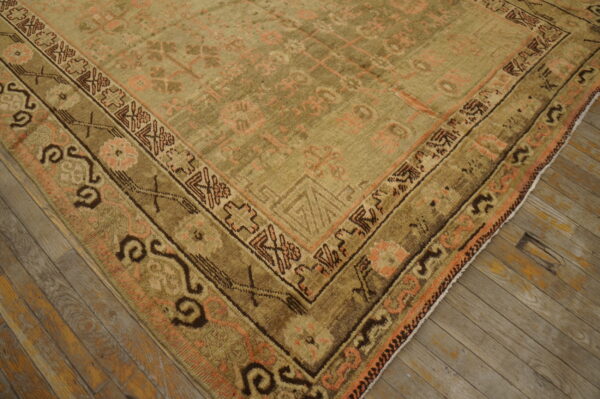 Muted olive rug with geometric coral and brown border patterns on distressed wood planks.