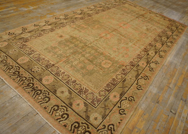 Low-pile traditional rug in muted olive, tan, and pink geometric patterns on distressed wood planks.