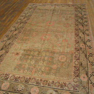 Rectangular, low-pile rug with faded tan, olive, and pink traditional patterns on a wood floor.