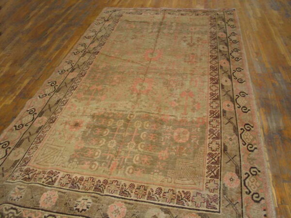 Rectangular, low-pile rug with faded tan, olive, and pink traditional patterns on a wood floor.