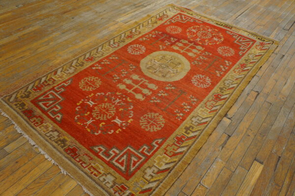 Geometric red rug with tan and brown motifs lies centered on distressed wooden plank flooring.