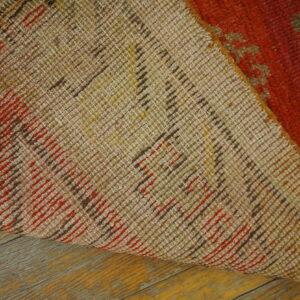 Close-up of a rug's tan woven backing and orange pile resting on distressed wood flooring.